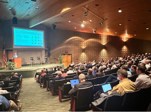 An auditorium full of people facing a projector screen.
